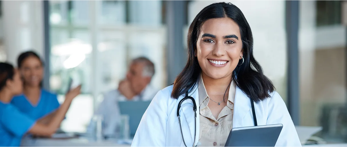 A female medical profession holds and iPad and smiles at the camera