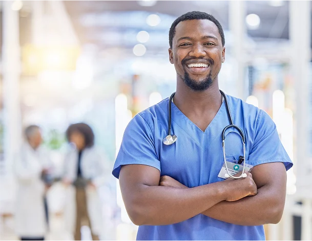 A male medical professional smiles while standing with his arms folded.