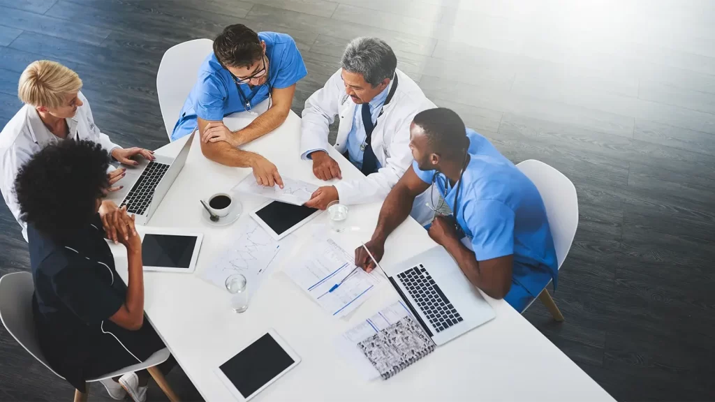 Team of medical workers sitting and meeting with laptops around table.