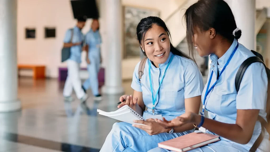 Asian nursing student and her female friend talk while studying in hallway at medical university.