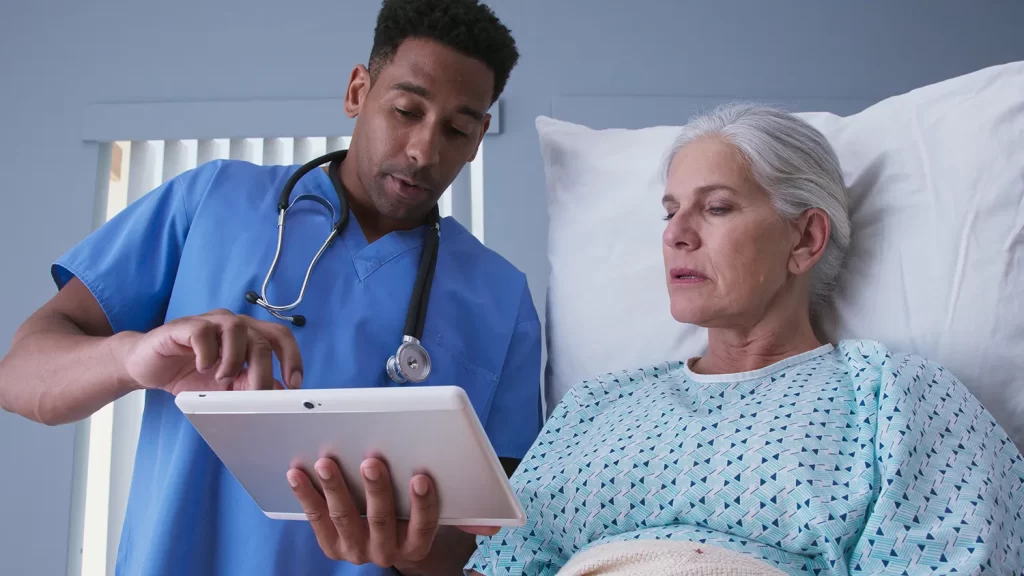 Male registered nurse showing ill elderly woman electronic pad