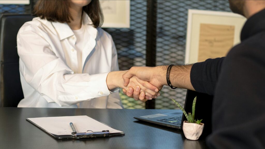 Two people shaking hands in front of a laptop